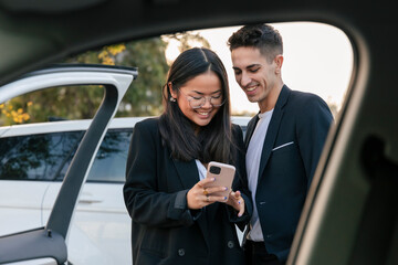 Smiling business colleagues sharing smart phone outside car