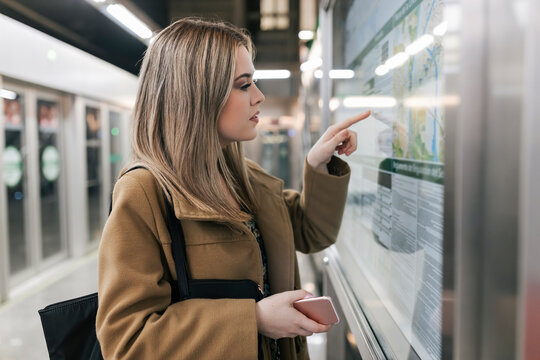 Woman with smart phone pointing at map in underground station
