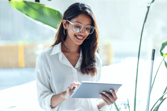 Smiling young businesswoman using tablet PC in front of window on sunny day