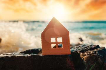 Idyllic landscape. Silhouette of a cardboard house on the shore ocean. Copy space. Concept of insurance and home purchase
