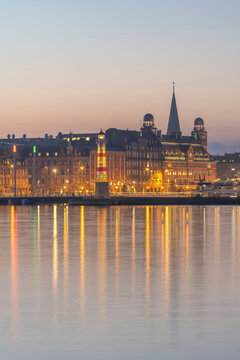 Sweden, Skane County, Malmo, Harbor lighthouse at dusk with bridge and Danske Bank in background