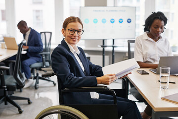 Side view portrait of successful businesswoman using wheelchair and reading documents at meeting table