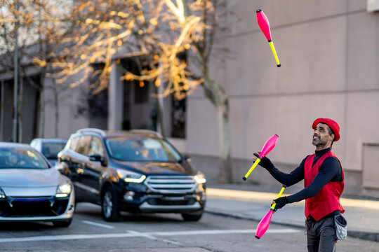 Street artist juggling pins in front of cars