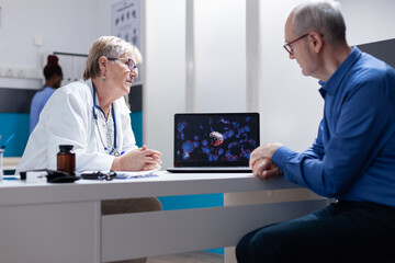 Doctor and patient discussing about illustration of coronavirus on laptop. General practitioner using computer to explain visual representation of covid 19 bacteria to senior man.