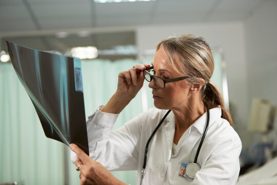 Female doctor holding eyeglasses examining X-ray in medical room