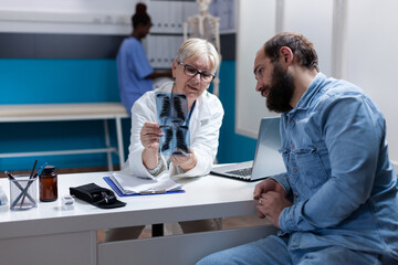 Medic holding x ray scan results for sick patient at checkup visit, explaining diagnosis and disease. Woman doctor analyzing radiography with man, giving medical addvice and support.