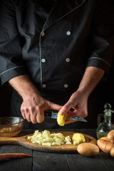 The chef cuts raw potatoes into pieces with a knife before preparing breakfast or dinner. Close-up of a cook hands while working in a restaurant kitchen.