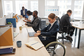 Side view portrait of smiling businesswoman using wheelchair while working with colleague in...
