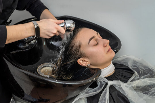 master colorist on his working day in a salon washes the mask from the client's hair.