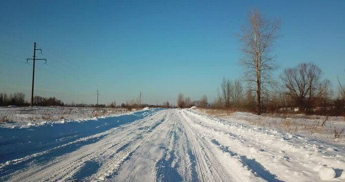 The drone flies low over a snowy road. Blue sky. Evening, sunny.
