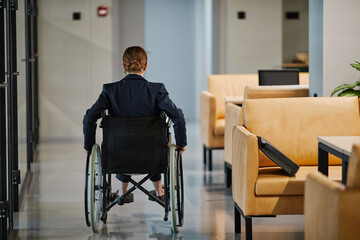 Full length portrait of successful businesswoman using wheelchair in office while moving towards camera, copy space