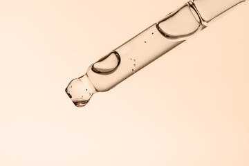 Transparent pipette with cosmetics on a beige background.