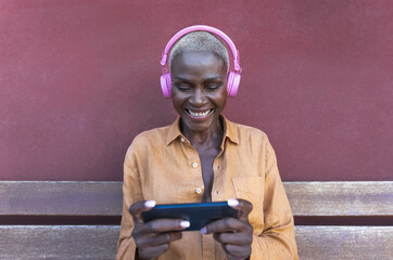 Happy African woman using mobile smartphone while listening music with wireless headphones