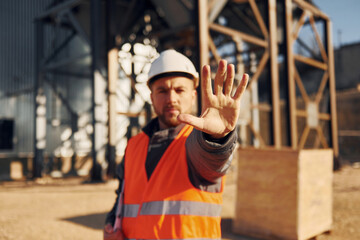 Natural lighting. Construction worker in uniform is outdoors near the factory