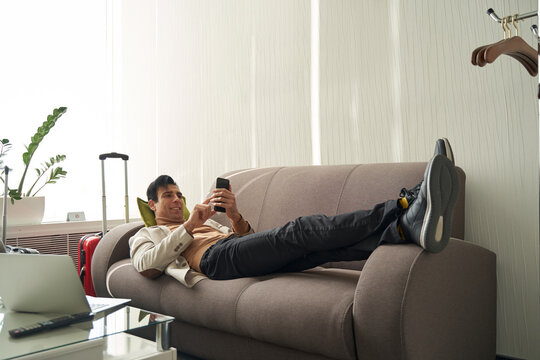 Man tapping on smartphone screen while resting on sofa