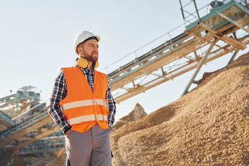Heavy transport behind. Construction worker in uniform is on the quarry