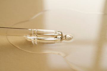 Pipette with oil or serum on a golden background.