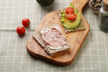 Healthy crunchy crisp bread sandwich with chicken pate, cream cheese, avocado and cherry tomatoes on wooden board