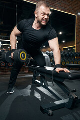 Fototapeta na wymiar Professional sportsman performing single-arm bent-over row in gym