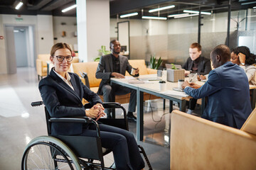 Portrait of successful businesswoman using wheelchair at meeting and looking at camera smiling