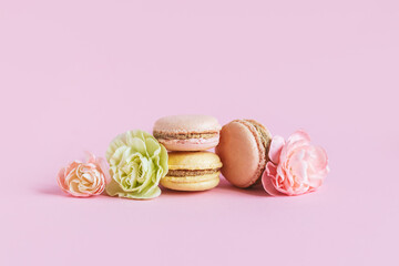 Tasty french macaroons with tender flower on a pink pastel background.