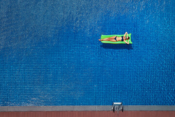 Enjoying suntan. Vacation concept. Top view of slim young woman in bikini on the green air mattress...