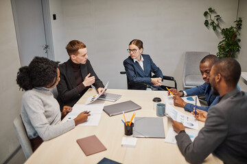 Fototapeta premium High angle portrait of successful businesswoman using wheelchair while leading meeting with team in office