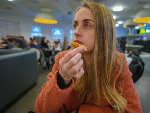 Woman eating chicken by hands on food court in mall