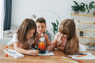 Building volcano from plasticine. Kids having fun in the domestic room at daytime together © standret