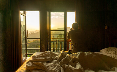 Asian male tourist sits in bed and takes pictures of tea plantations in the morning, Chiang Rai, Thailand.