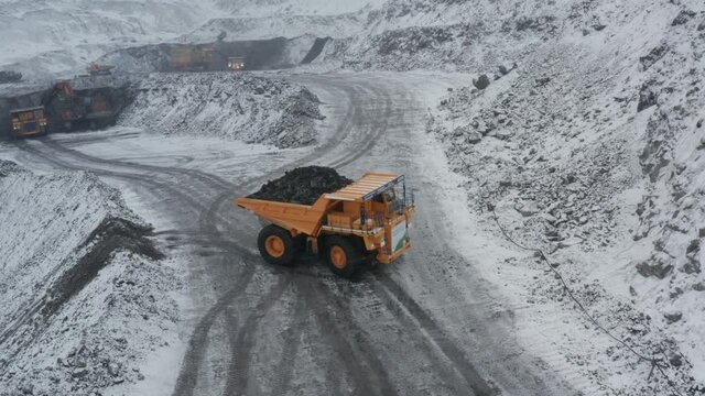 Large quarry dump trucks loaded with coal work at the coal mine in heavy snowfall.