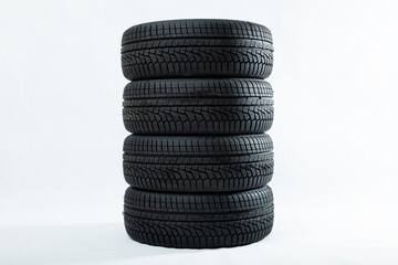 Fototapeta na wymiar Stack of winter tires with specific structure and deep ridges shot in studio. Black rubbers for car piled on top of each other isolated on white background. Four driving wheels with copy space.