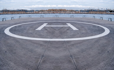 Helipad sign, yellow color letter H on the ground. Helicopter landing area by the sea