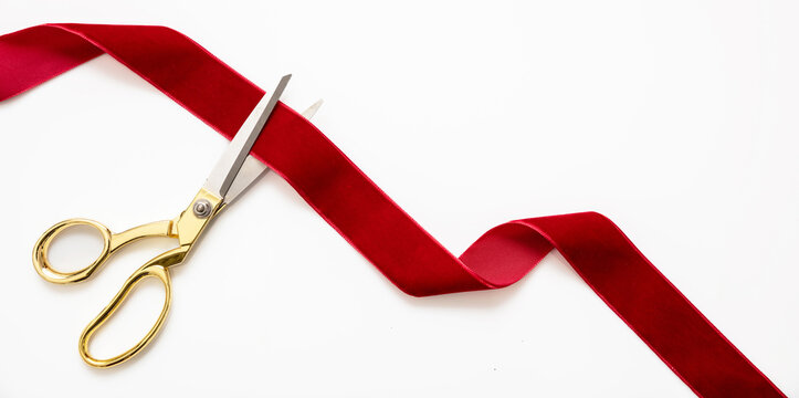 Grand opening, ribbon cut, overhead of gold scissors and red velvet ribbon isolated on white