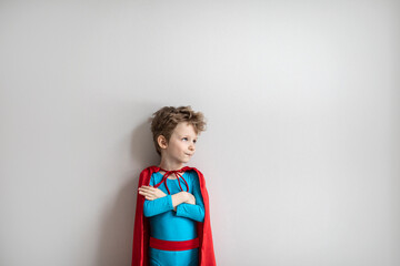 Little child play superhero. Dreamy boy in blue superhero costume and red cape
