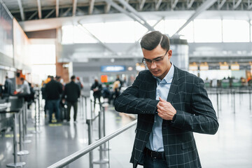 Taking out the documents. Young businessman in formal clothes is in the airport at daytime