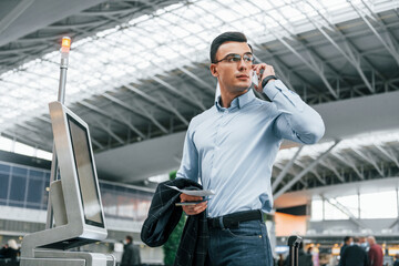 Standing by the terminal. Young businessman in formal clothes is in the airport at daytime