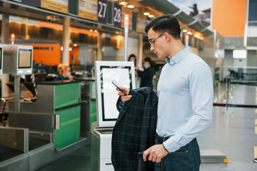 Holding phone. Young businessman in formal clothes is in the airport at daytime