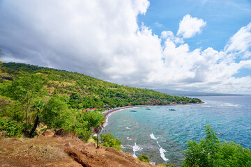 Fototapeta premium Beautiful landscape with ocean shore, green hill, cloudy sky. Amed Beach, Bali Island, Indonesia.