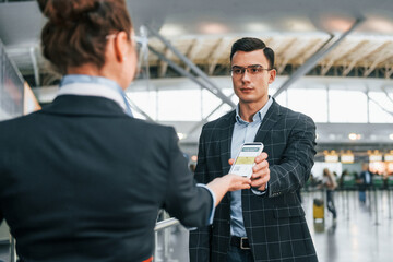 Fototapeta na wymiar Holding and showing vaccination certificate. Young businessman in formal clothes is in the airport at daytime