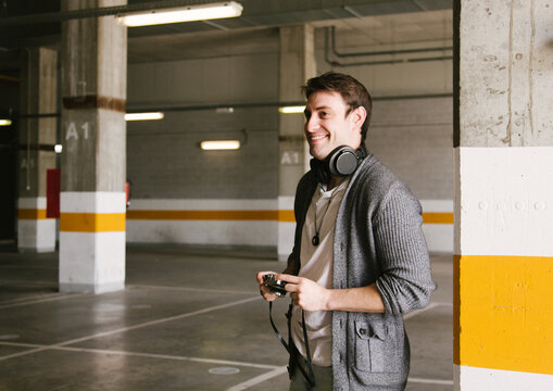 portrait of fashionable cool man on an industrial environment listening to music with earphones. holding a retro camera. High quality photo