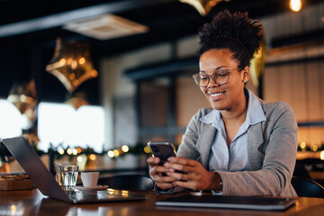 Business African woman, looking at her phone, waiting for her food to arrive.