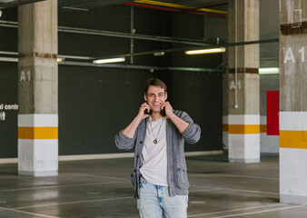 portrait of fashionable cool man on an industrial environment listening to music with earphones in his hands. High quality photo