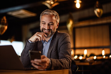 Smiling caucasian man, comparing notes on his laptop, with notes on his phone.