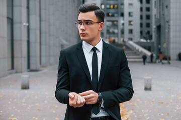 Portrait of businessman that is in black suit and tie is outdoors in the city