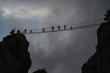 Silhouettes of people passing a dangerous suspension bridge on the top of Ai-Petri Mountain in...