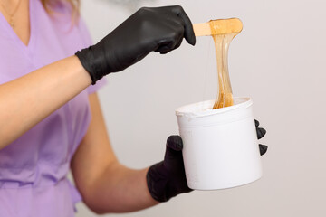 close-up. Hands in black rubber gloves hold a bucket of  sugar paste or wax for depilation