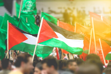 Palestine flags waved by Palestinian people in the air with Hamas flags in the background