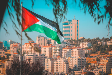 Palestine flag as through the tree leaves with some city buildings on the background at ramallah