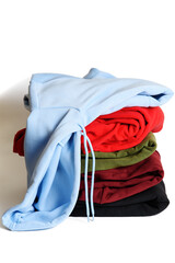 Folded hoodies and hooded sweatshirts on white background. Light blue hoodie on top of stack. Trendy comfortable casual clothes. Closeup. Vertical orientation.